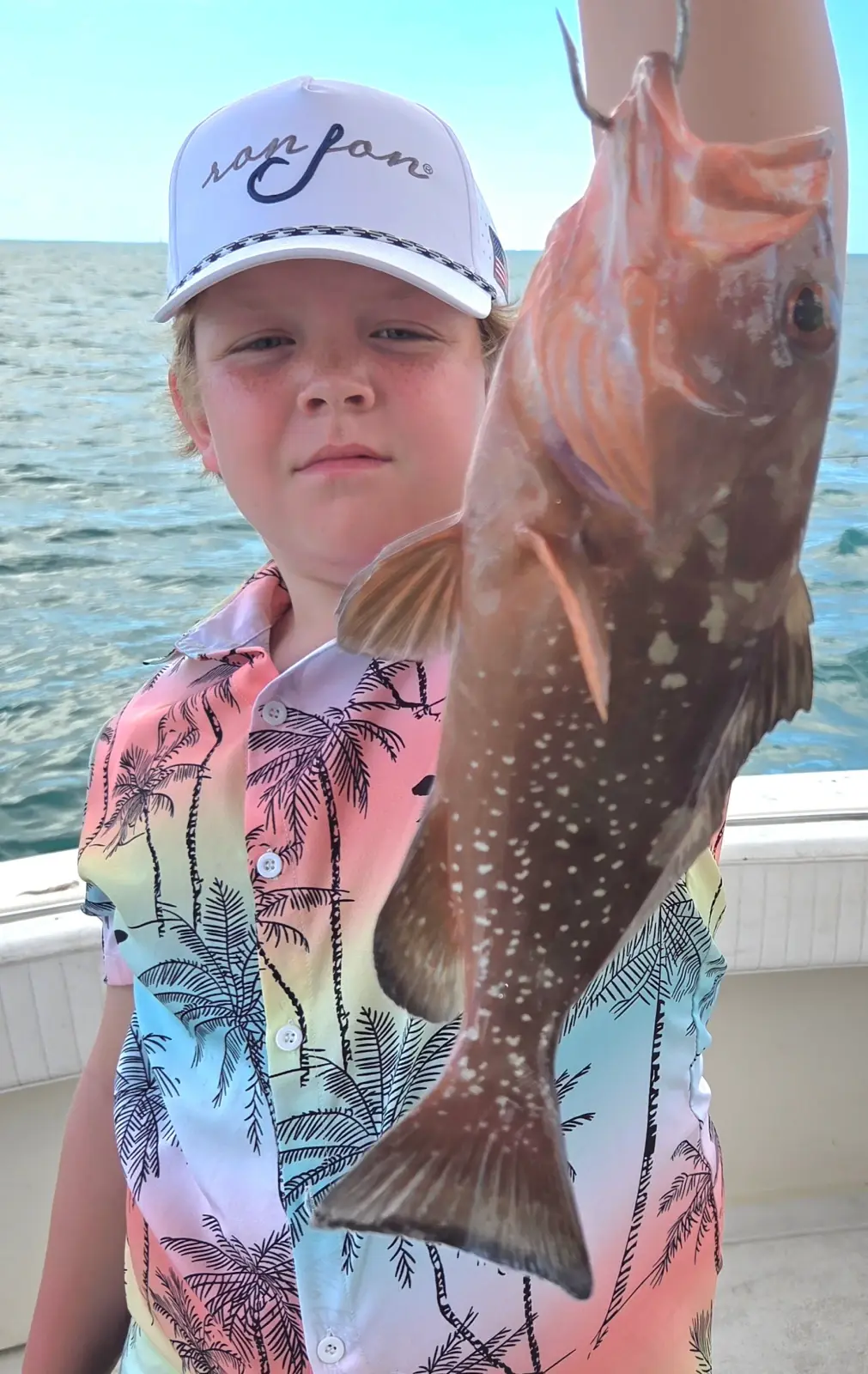 A young angler holding a grouper aboard the Magic