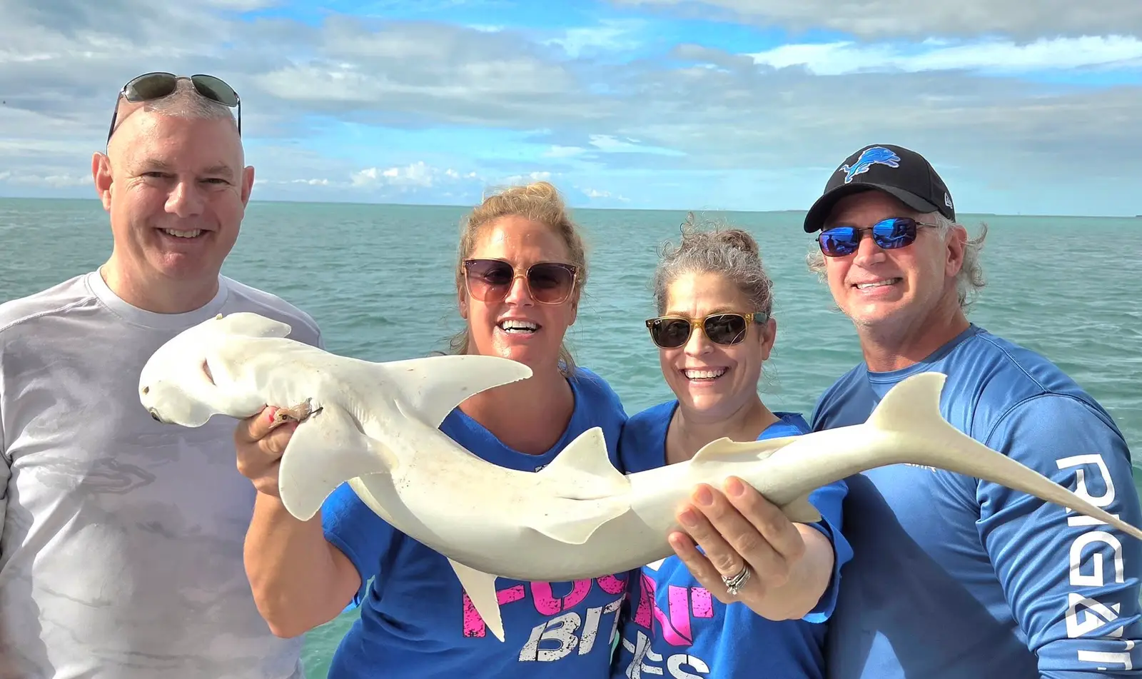 A group of four guests holding a shark caught on a half day charter in Key West